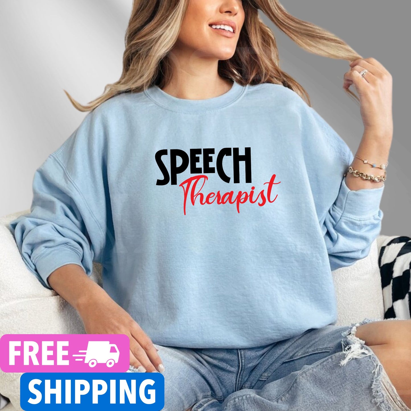 Person wearing a baby blue Speech Therapist statement clothing crew neck sweatshirt with bold black and red text, standing in a modern interior setting.