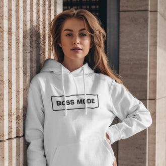 A woman wearing a white BOSS MODE hoodie leaning casually against a modern stone wall.