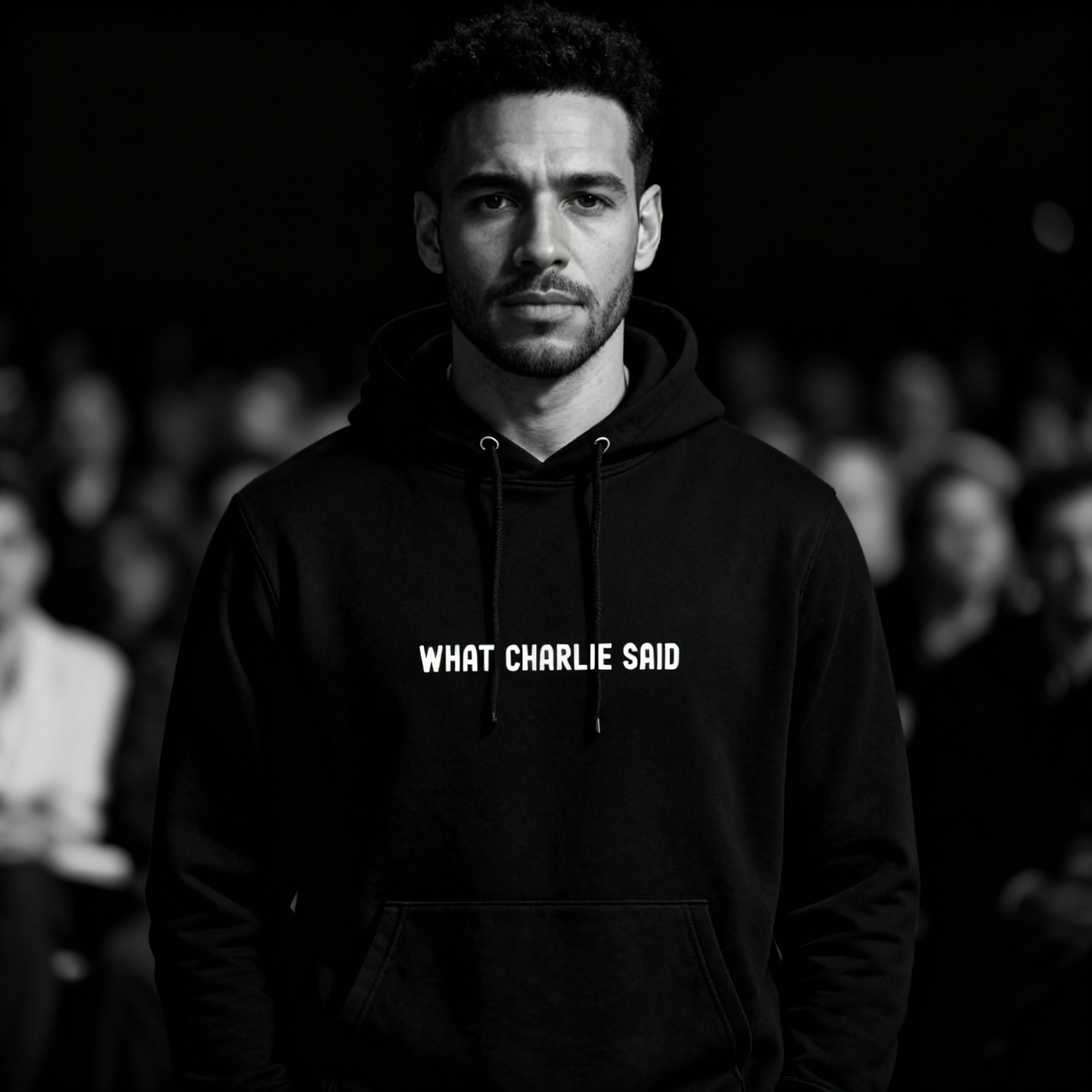 Model wearing the “What Charlie Said” black hoodie by Yebber, standing confidently among a blurred crowd – statement clothing that stands for truth.