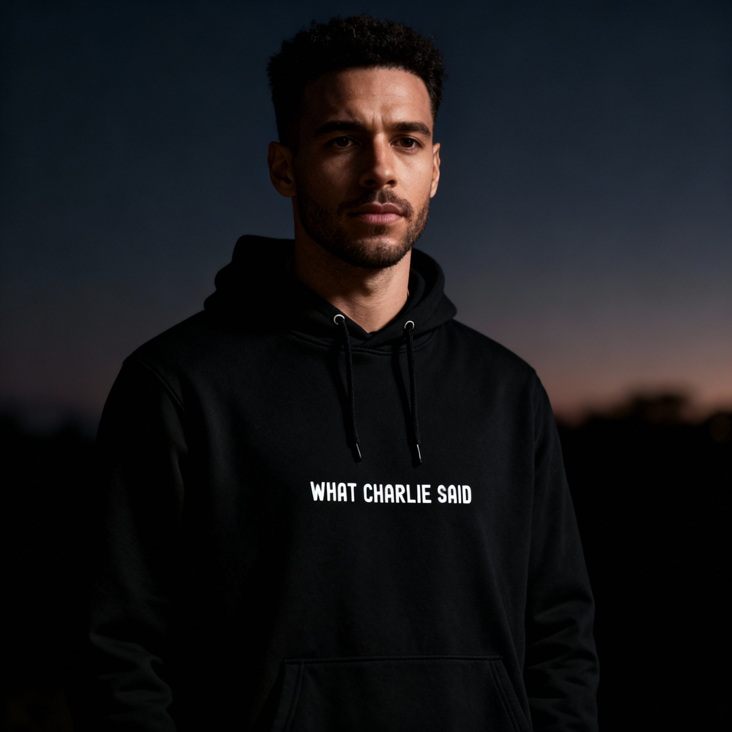 Man wearing the black “What Charlie Said” hoodie by Yebber at dusk – minimalist statement clothing with bold white text.