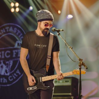 Person playing guitar wearing a black FUNK OFF T-shirt from Yebber, featuring bold typography with a witty design – statement clothing for music lovers and free spirits.