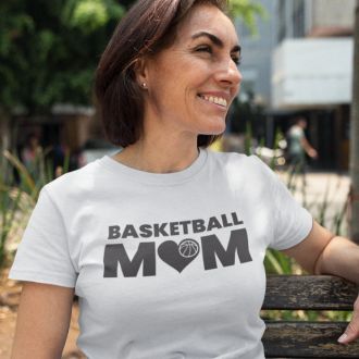 Smiling woman outdoors wearing a white Basketball Mom Pride T-shirt from Yebber, featuring bold text with a basketball graphic – statement clothing for proud sports moms.