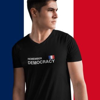 Person wearing a black Remember Democracy France statement clothing T-shirt with white text and a small French flag, standing in front of a large French flag background. 