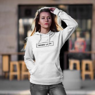 Successful woman wearing a white Boss Lady statement clothing hoodie with bold black text, posing confidently outdoors with a modern café setting in the background. Premium DTG print quality, fast delivery, and free worldwide shipping by Yebber