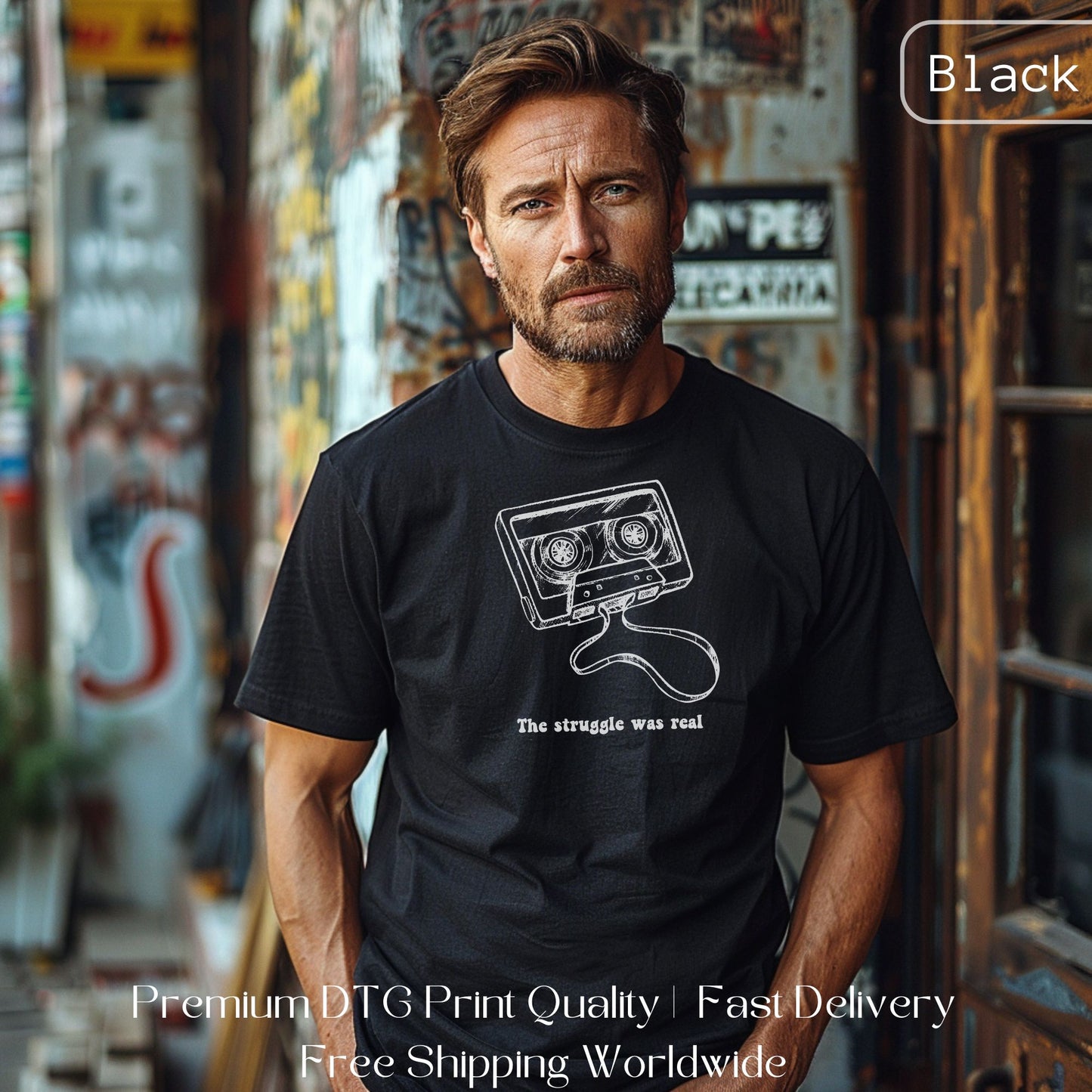 Man wearing a black Gen X statement clothing T-shirt with a white cassette tape design and the text "The struggle was real," standing against a graffiti wall. Premium DTG print quality, fast delivery, and free worldwide shipping by Yebber.