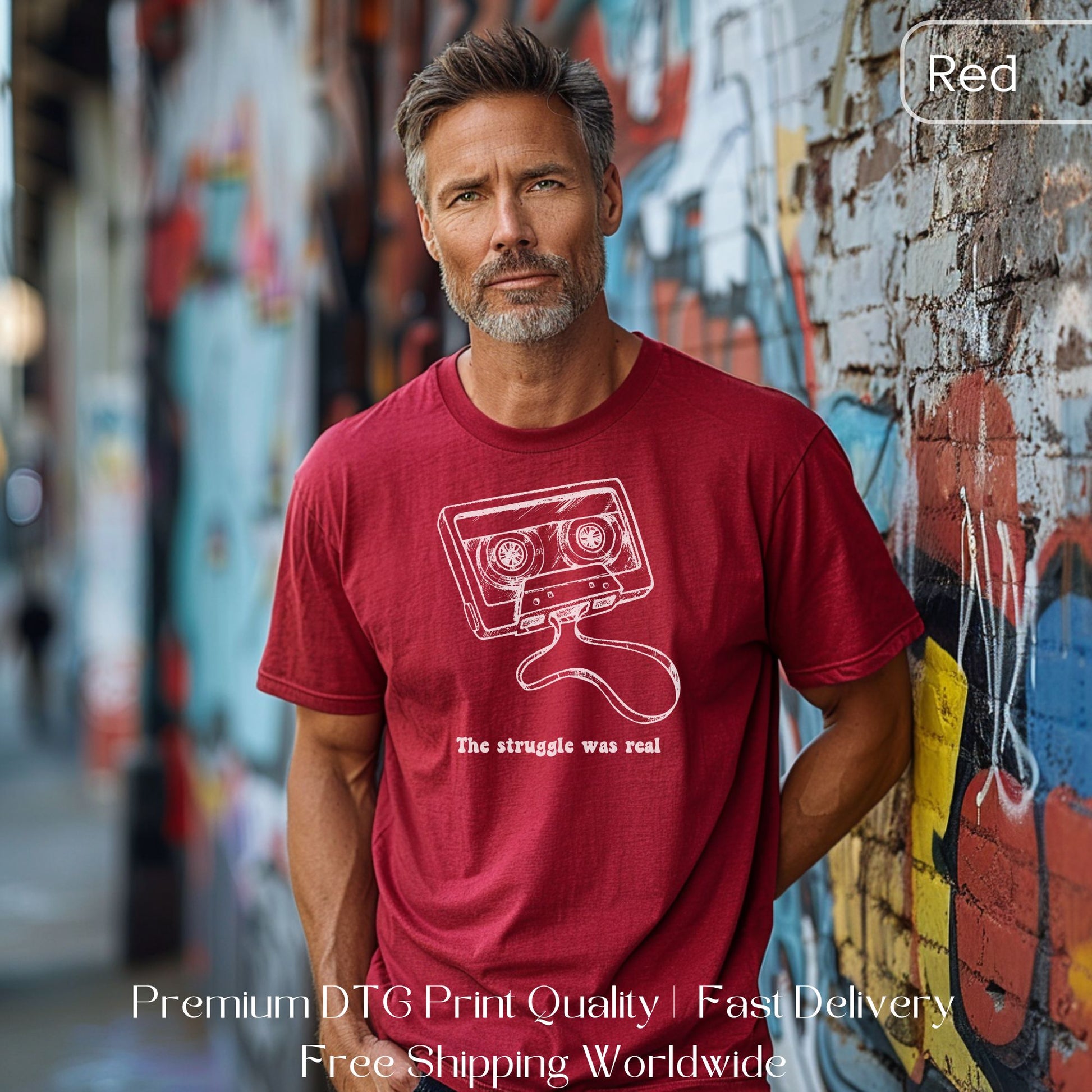 Man wearing a red Gen X statement clothing T-shirt with a white cassette tape design and the text "The struggle was real," standing against a graffiti wall. Premium DTG print quality, fast delivery, and free worldwide shipping by Yebber.