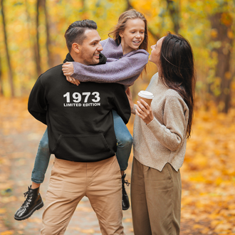Man wearing a black hoodie with white bold text 1973 limited edition with his family in a park on a fall day